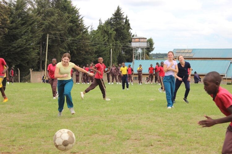 Volunteers and young people playing football together on a field in Kenya